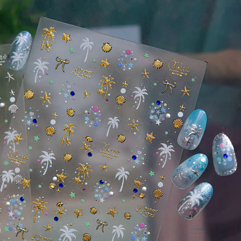 Nail art stickers with palm trees, shells, and stars on a clear sheet, with a hand displaying nails with blue and silver nail art in the background.