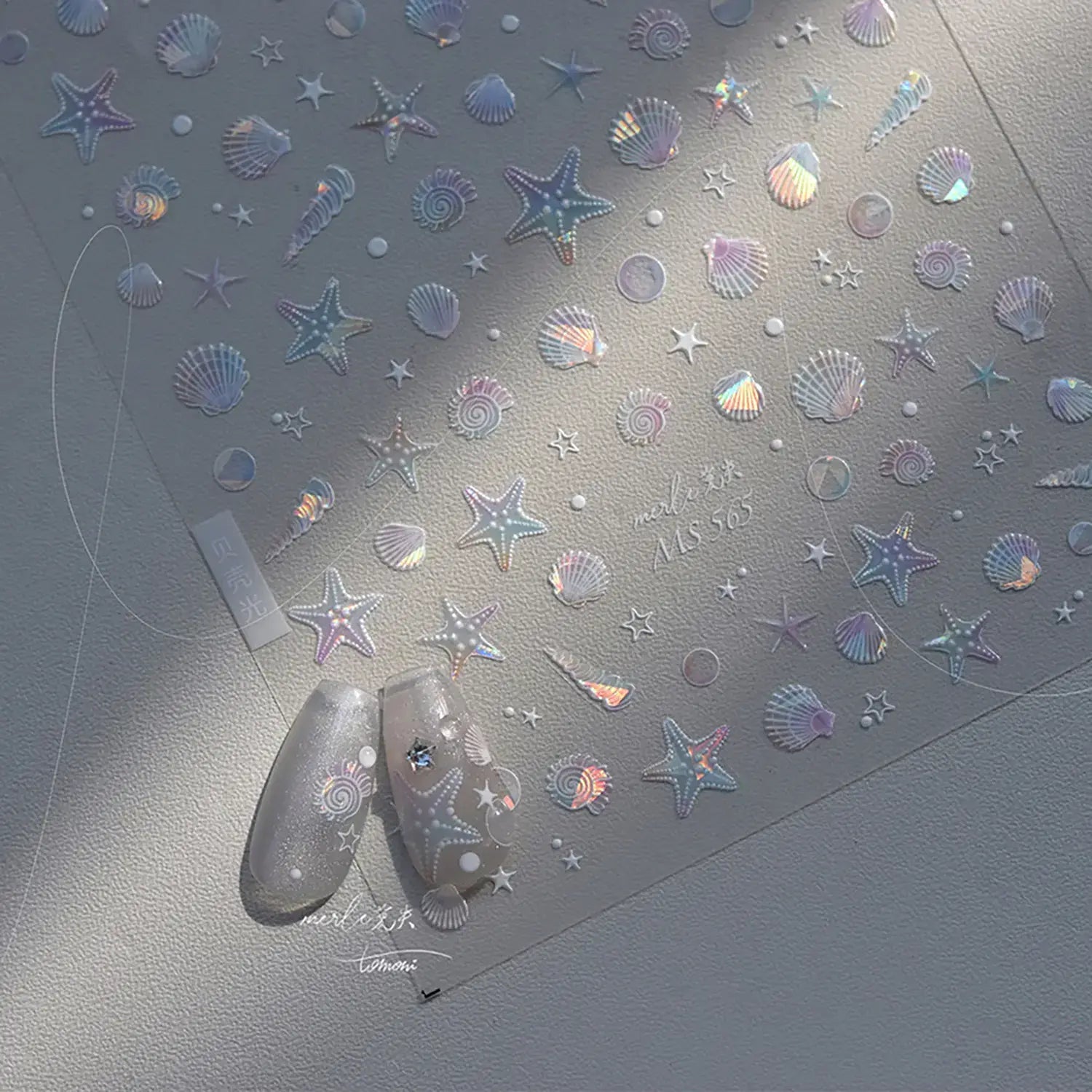 Nail art stickers with starfish and shell designs on a gray surface.