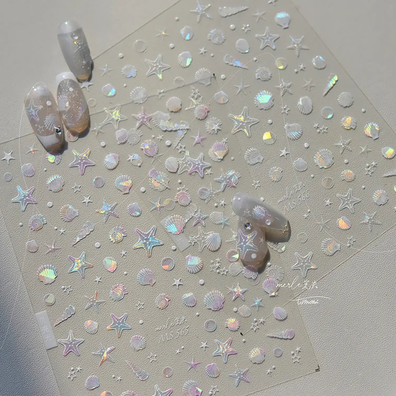 Sheet of star and shell-shaped nail art stickers on a light gray background with two nails featuring the design.