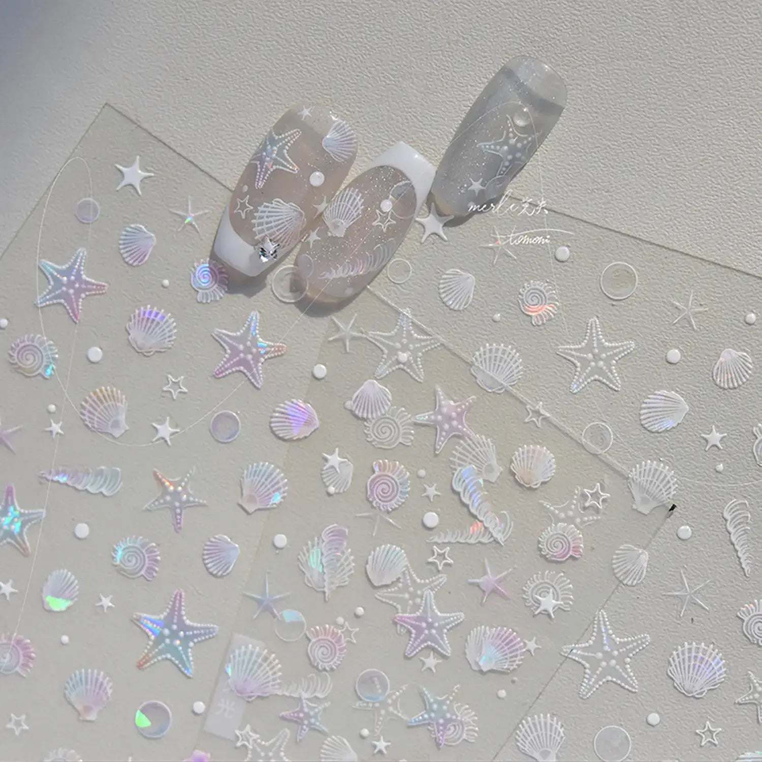 Nail art stickers with starfish, seashells, and moons on a light gray background